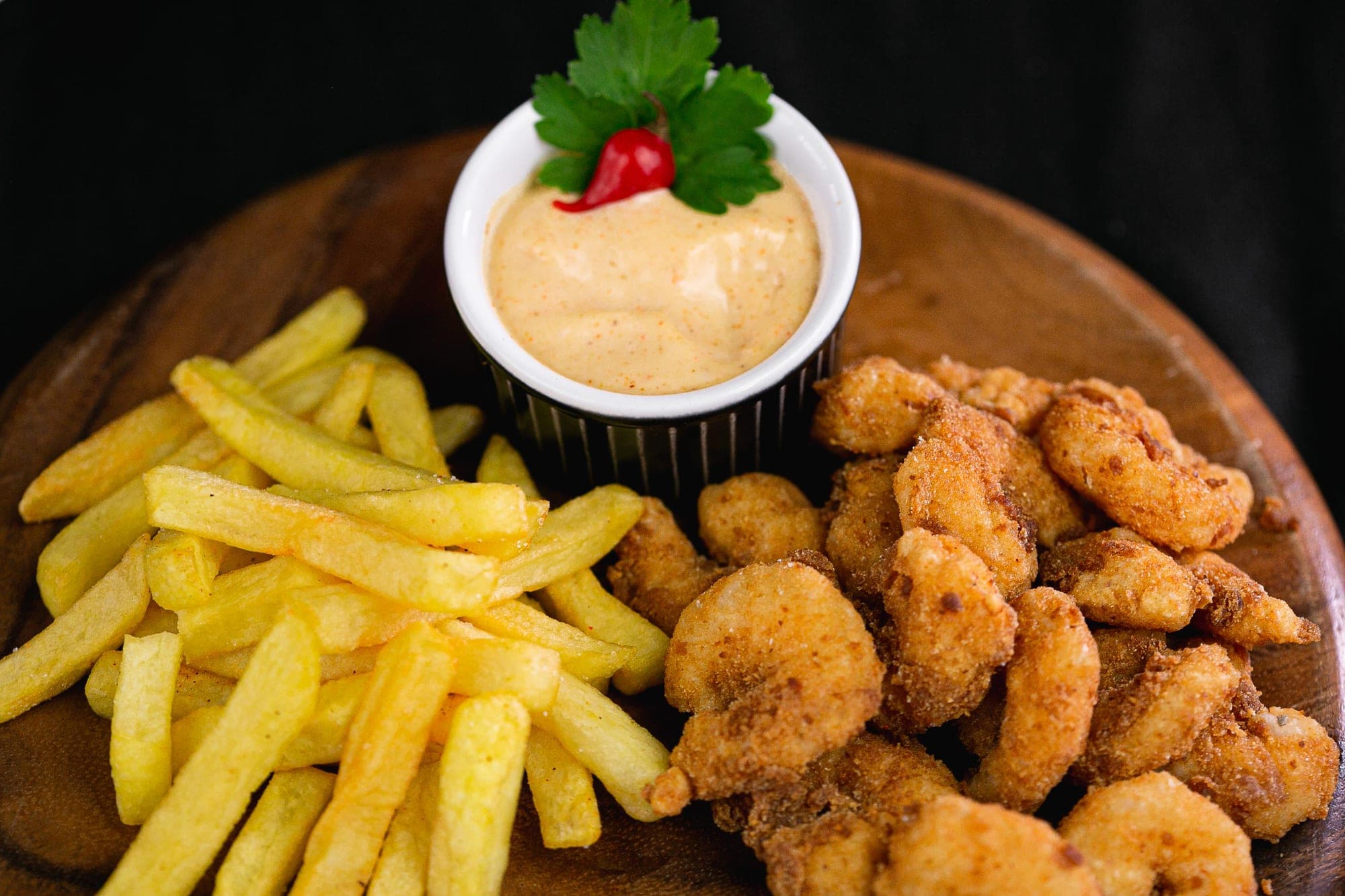 Iscas de camarão empanado, batata frita e molho da casa em tábua de madeira