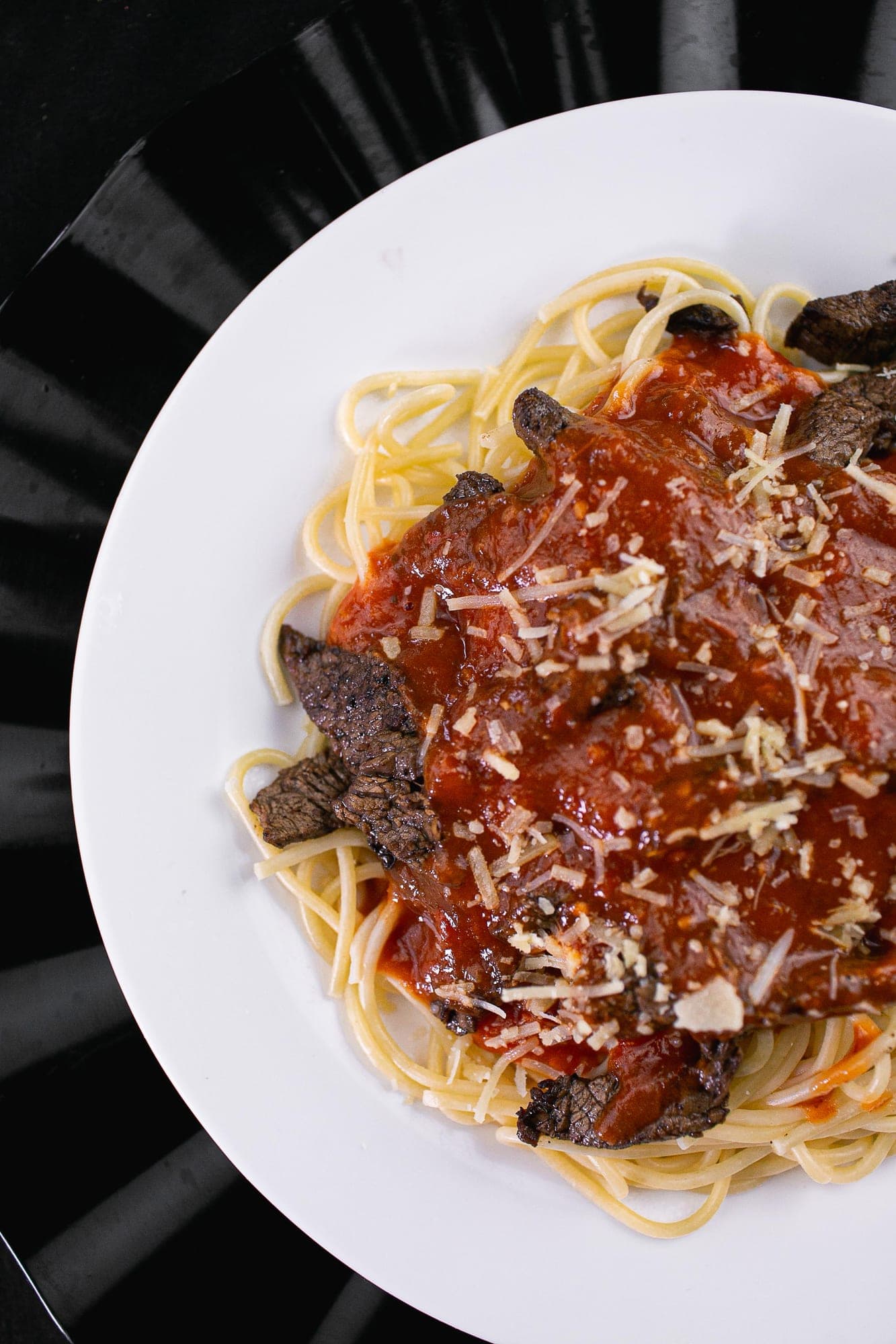 Espaguete com tiras de carne grelhada, molho de tomate caseiro e queijo ralado em prato branco